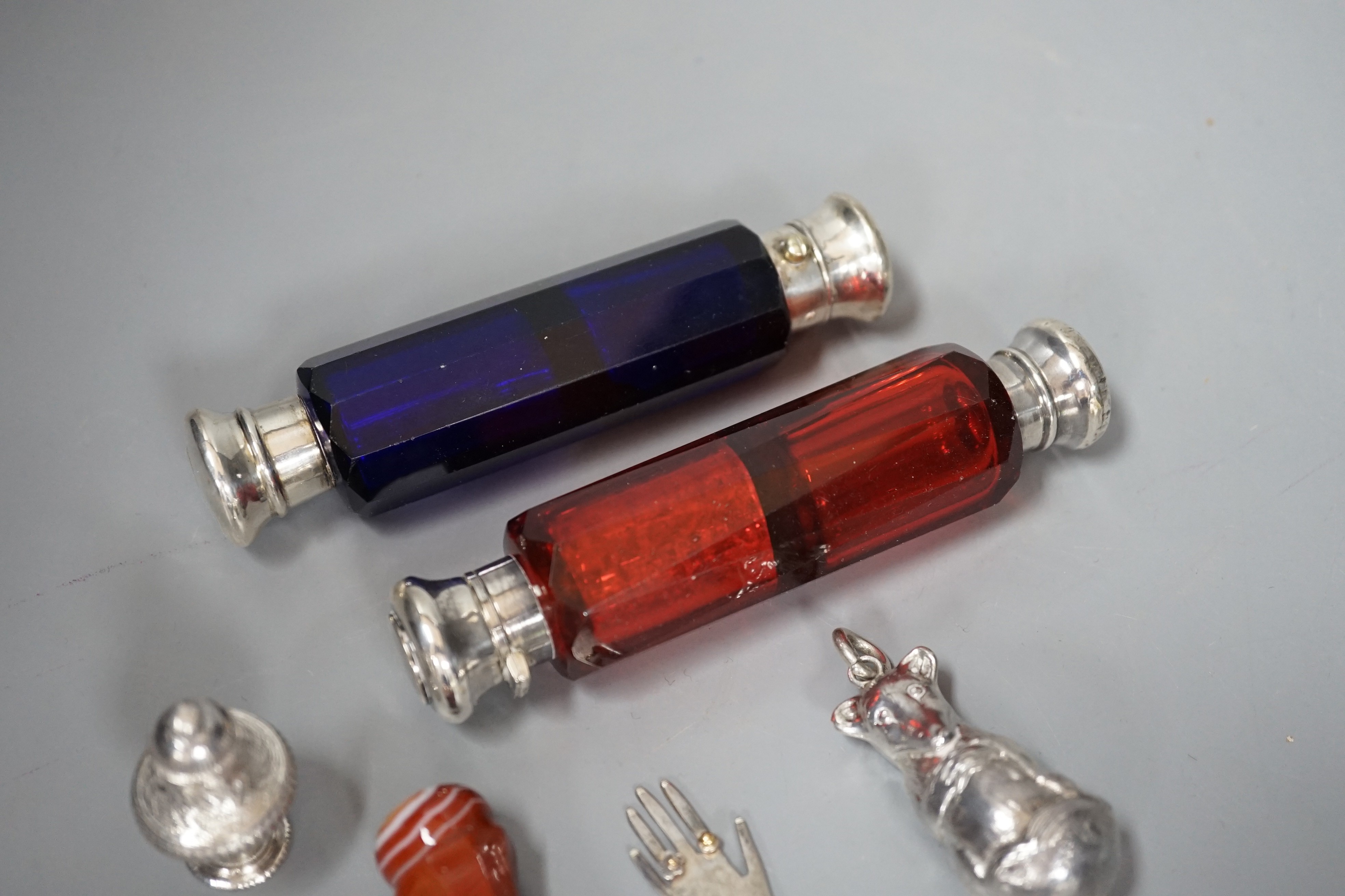 Two Victorian white metal mounted ruby or blue glass double ended scent bottles, 12.5cm, an agate mounted seal, a modern silver child's rattle, a continental scent/seal and a silver hand charm.